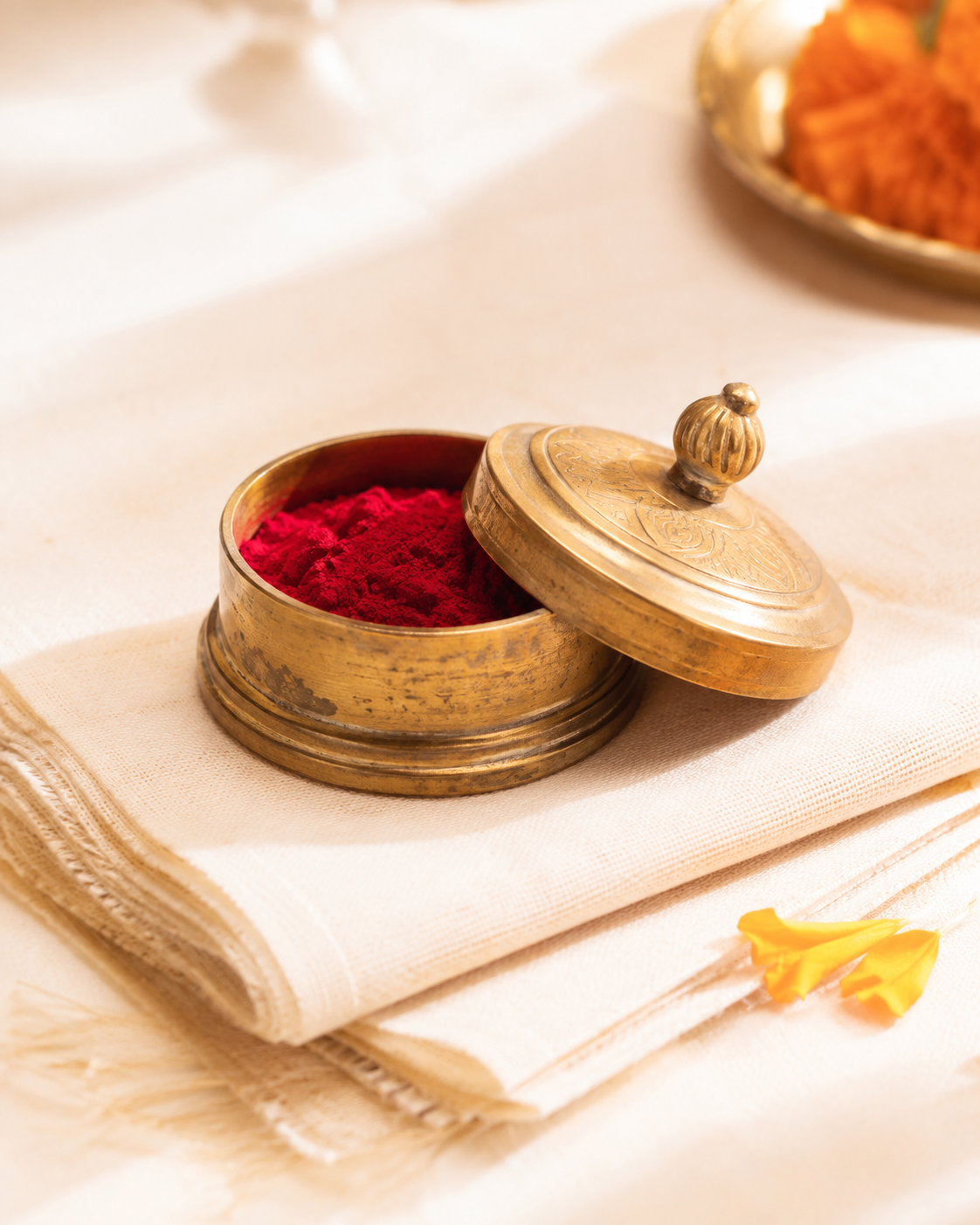 An antique brass kumkum box filled with red kumkum on ivory cloth